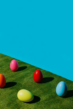 Multicolor eggs with one single egg laying on green grass against vibrant blue wall. Creative Easter holiday celebration concept. Traditional arrangement or greeting card with copy space for text.