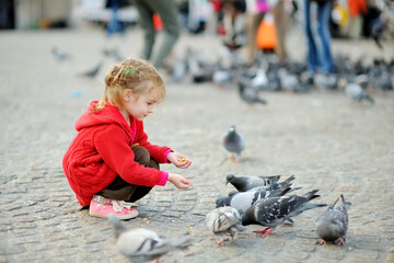Cute little girl feeding and chasing birds on Dam Square in Amsterdam on summer day.
