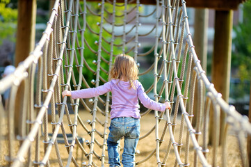 Adorable little girl having a good time climbing in adventure park.