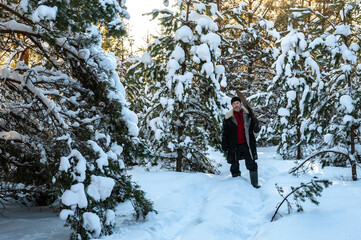 serious brutal man with beard and in warm unbuttoned sheepskin coat stands in middle of snow-covered forest. Man is holding hand saw on his shoulder
