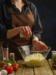 Macro shot. A professional chef adds spices to grated cheese on a dark background. The concept is cooking dishes with cheese - pizza, pie, salad. Recipes for restaurant and home cooking.