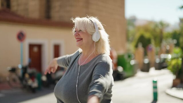 Middle age blonde woman listening to music using smartphone and dancing at street