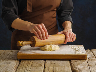 Close-up. The chef rolls out the dough with a rolling pin on a wooden table, a cutting board. Recipes for dough products - pizza, pasta, confectionery. Restaurant, hotel, food blog.