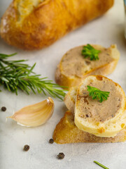 Gourmet food. Slices of fresh French baguette with fragrant foie gras, decorated with parsley leaves, sprigs of rosemary, garlic on a white background. Macro shot. Delicious healthy food.