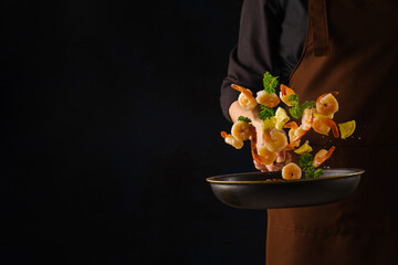 Chef in uniform prepares shrimp seafood with herbs and lemon in frozen flight on a frying pan on a...