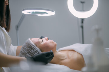 Young woman on a cosmetology facial skin care procedure in a beauty salon. Cosmetologist and...