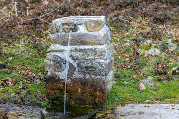 Stone fountain with a long drinking spout on the side of the mountain