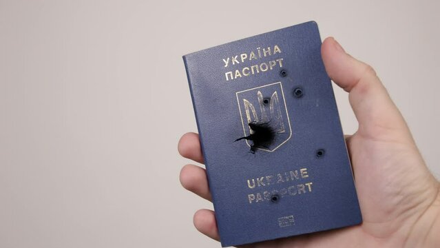 Man's hand holds a passport of Ukraine shot with bullets. Concept of war in Russia against Ukraine. Aggression of occupiers, genocide of the people