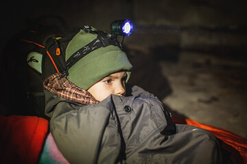Thoughtful little boy with headlamp lays in a bomb shelter and waits for the end of the air attack...