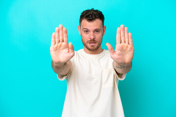 Young Brazilian man isolated on blue background making stop gesture and disappointed