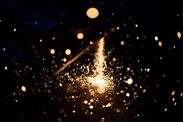 Obraz premium Sparks from grinding metal. Steel processing in workshop. Lights in dark. Production of parts. Cutting became grinder.