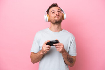 Young Brazilian man playing with video game controller isolated on pink background and looking up © luismolinero