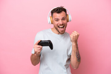Fototapeta na wymiar Young Brazilian man playing with video game controller isolated on pink background celebrating a victory in winner position