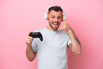 Fototapeta na wymiar Young Brazilian man playing with video game controller isolated on pink background making phone gesture. Call me back sign