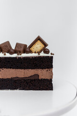 Chocolate cake with cream sponge cake decorated with cookies stands on a white stand on a white background. Isolated background. A tasty treat for a children's birthday party. Pastry craftsmanship.