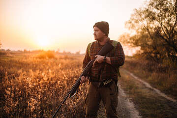 Young strong soldier with riffle and ammunition belt moving outdoors by the dirt road in sunset time