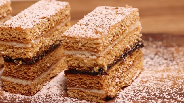Traditional homemade Romanian Honey Layered Cake with plum jam and semolina cream also called Albinita or Dulcineea. Panning shot of cut portions of cake.
