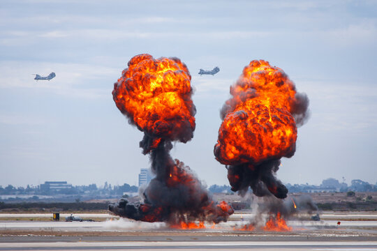 Bomb explosion at an airfield with combat helicopters in the background