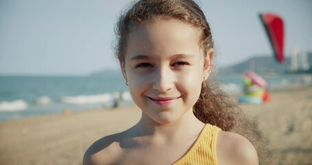 Portrait Funny happy little girl smiling child looking at camera cheerful enjoying warm summer vacation on seaside beach waterfront slow motion, cute kid child with pretty face.Concept happy childhood