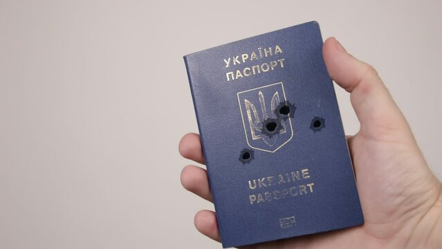 Holes in shot Ukrainian passport. Concept of occupation of the country, the war in Ukraine. Male hand holding a blue document. Russian aggression, occupiers