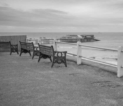 Black and white photo of the wooden benches on Cromer clifftop over looking the beach and famous Victorian era pier.