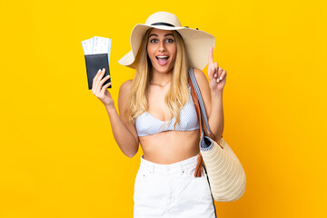 Young Uruguayan blonde woman in swimsuit holding a passport over isolated yellow background pointing up a great idea