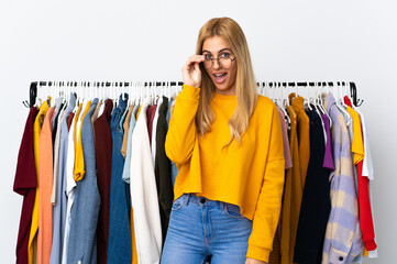 Young Uruguayan blonde woman in a clothing store with glasses and surprised