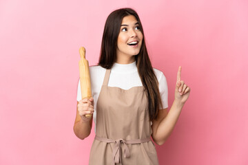 Teenager Brazilian girl holding a rolling pin isolated on pink background thinking an idea pointing the finger up