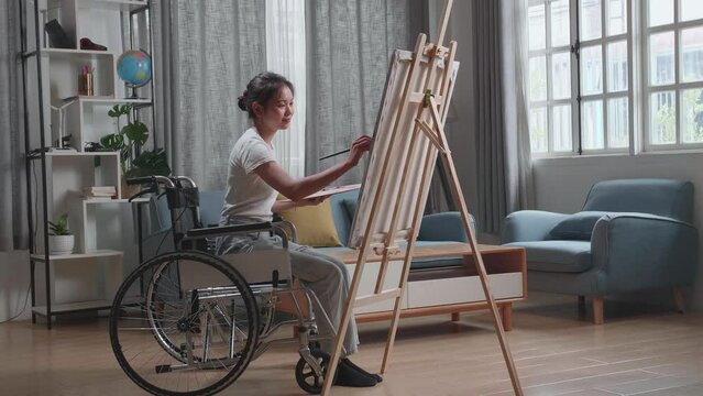 Asian Artist Girl In Wheelchair Holding Paintbrush Mixed Colour And Painting On The Canvas
