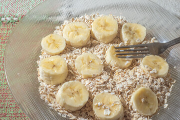 flaked oats and sliced banana, on a plate that is on a table with natural light,copy space in several parts