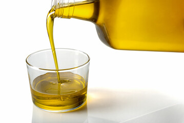Extra virgin olive oil being poured from bottle into glass cup on white background