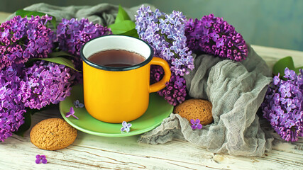 Fototapeta na wymiar Bouquet of lilac, the mug and the cookies on the wooden background, selective focus.