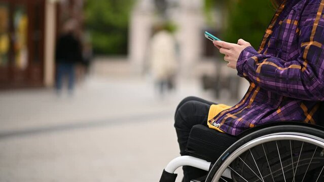 Woman with disability who uses a wheelchair using a smartphone while out in the city