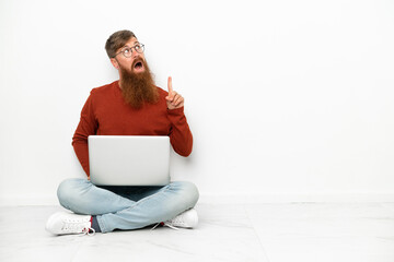 Young reddish caucasian man with laptop isolated on white background thinking an idea pointing the finger up