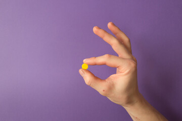 Man's hand holds a yellow round pill with his fingers. Very peri color background. Daily dose of...