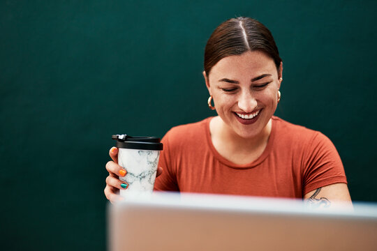 Coffee gets me through the busy day. Cropped shot of an attractive young businesswoman sitting alone and using her laptop while holding a cup of coffee.