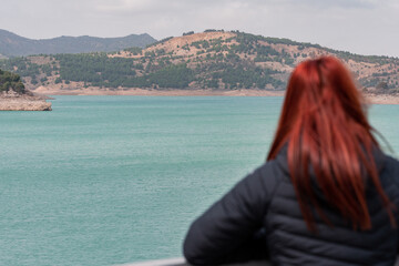 Fototapeta na wymiar unrecognisable red-haired woman observes reservoir with turquoise water