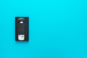 Retro video tape over turquoise blue background with copy space. Old black videocassette flat lay top-down composition.
