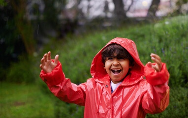 Hes sort of singing in the rain. Shot of a little boy wearing a raincoat playing outside.