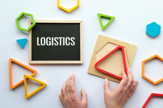 Text Logistics on blackboard. Nested wood triangles in rainbow colors, human hand. Geometric education stacking puzzle. Montessori sensory toy. Flat lay on white paper background.