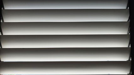 Obraz premium White wooden blinds pattern,sunlight from out side shining to blinds on window.