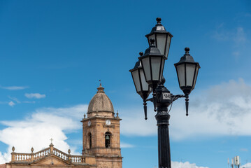 Fototapeta na wymiar Old street lamp with bell tower of the church in the city Tunja. Colombia.