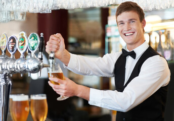 Well drink to that. Happy young barman preparing beer on tap with a smile.