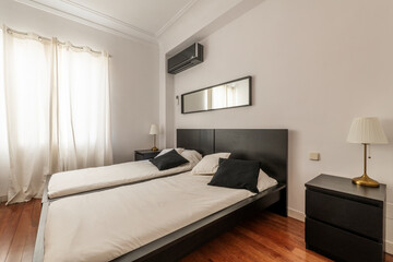 Bedroom with double beds, dark wood headboard, long mirror above the headboard, air conditioner, black cushions and built-in wardrobe with cherry sliding doors
