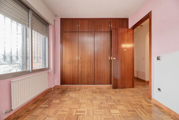 Fototapeta premium Empty vintage bedroom with aluminum radiator, built-in wardrobe with four wooden doors, oak parquet flooring and pink painted walls