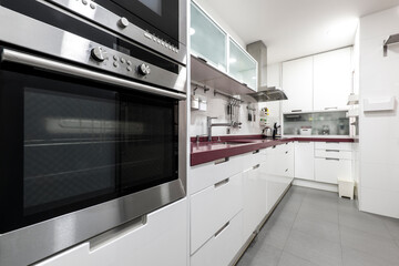 Long kitchen with white lacquered furniture, red countertop and stainless steel appliances