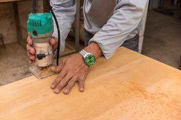 A carpenter uses a wood trimmer to chamfer to edge of a table. Compact Wood Palm Router Tool. At a...