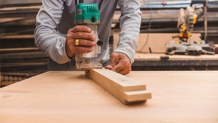 A carpenter uses a wood trimmer to chamfer to edge of a table leg. Compact Wood Palm Router Tool. At a furniture making workshop.