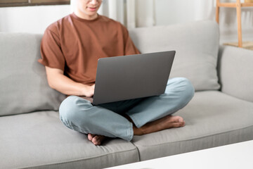Technology Concept The male who is wearing casual clothes sitting on the sofa, resting his notebook on his lap and doing his work