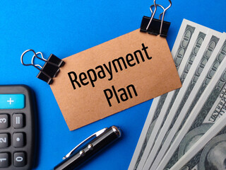 Top view calculator,pen,banknotes and brown card with text Repayment Plan on blue background.